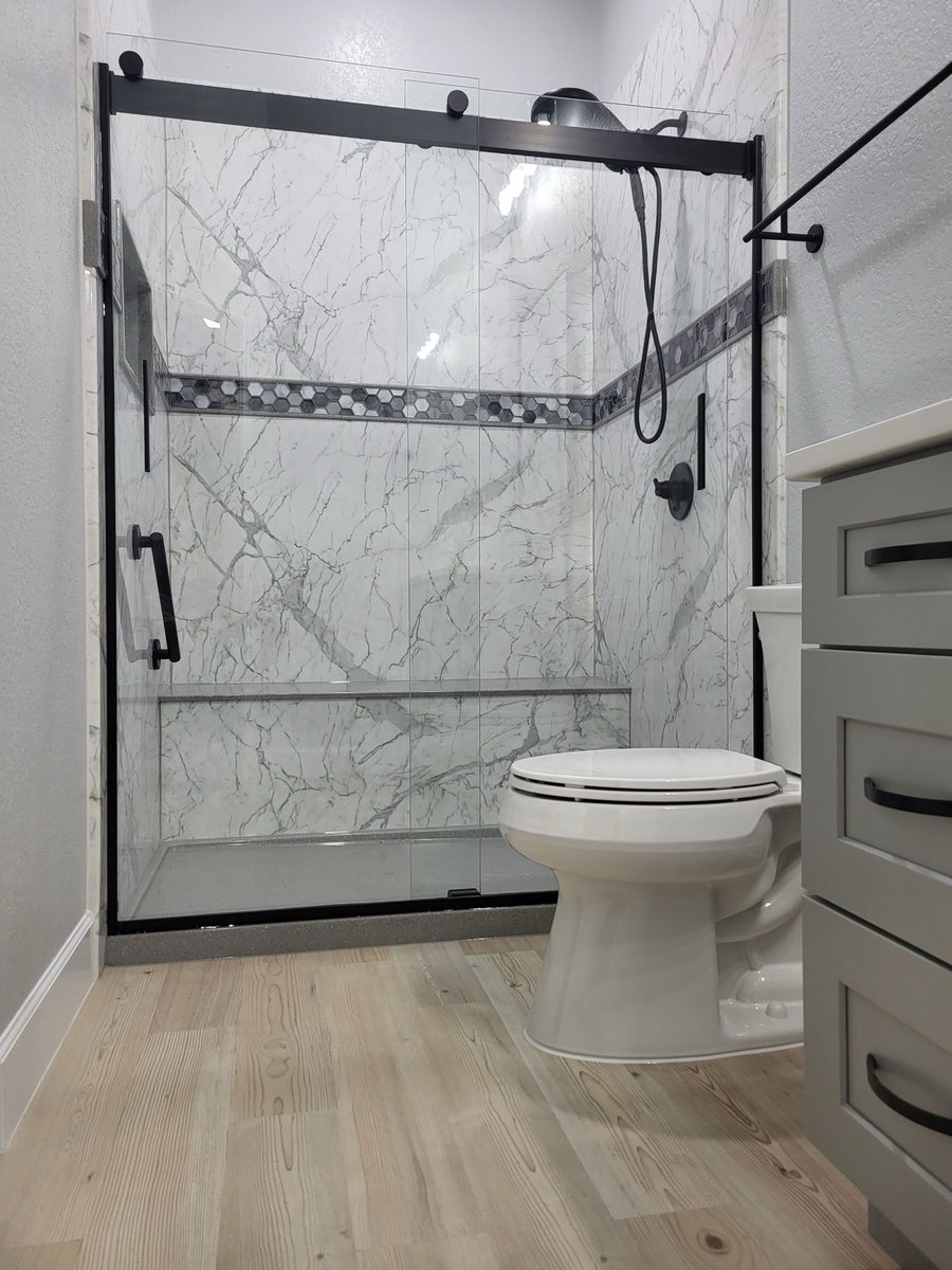 Marble walk-in shower with sliding glass door beside white toilet on wood-look floor