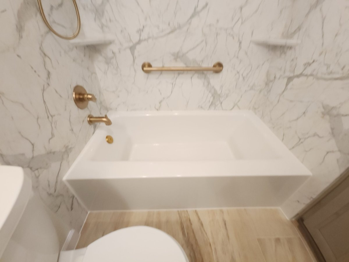 White soaking tub with brushed gold fixtures against marble-look wall panels