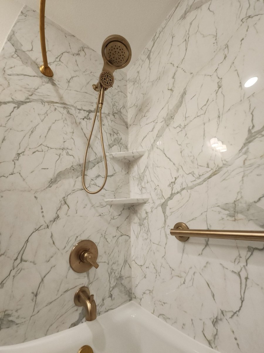 Marble-look shower walls with brushed gold handheld showerhead and corner shelves