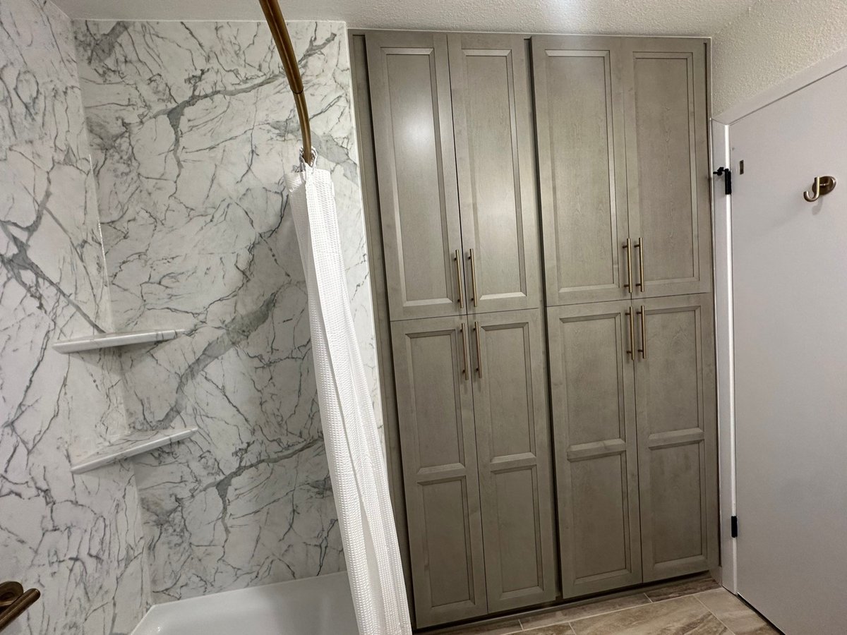 Marble-look tub surround with white curtain beside gray floor-to-ceiling storage cabinets