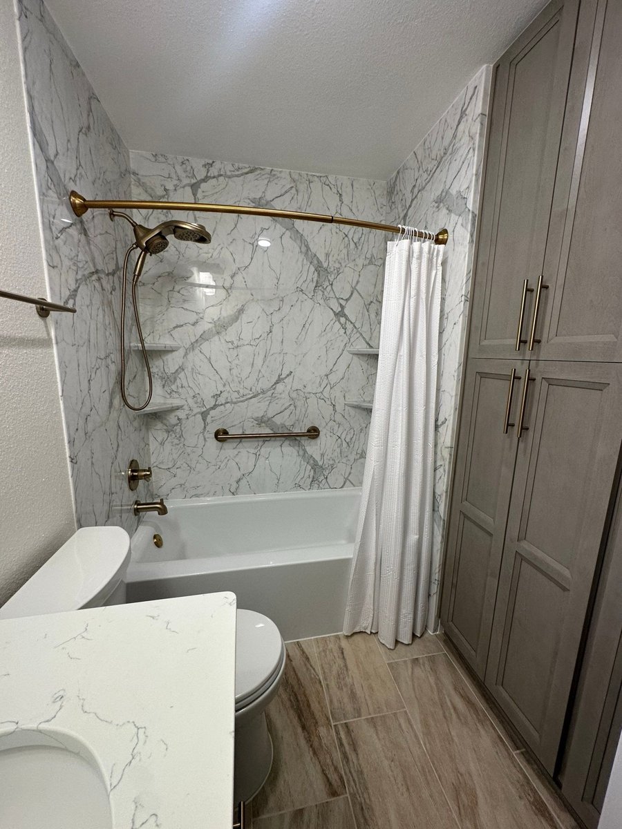 Guest bath with tub-shower, marble walls, gray cabinets, and wood-look tile floor