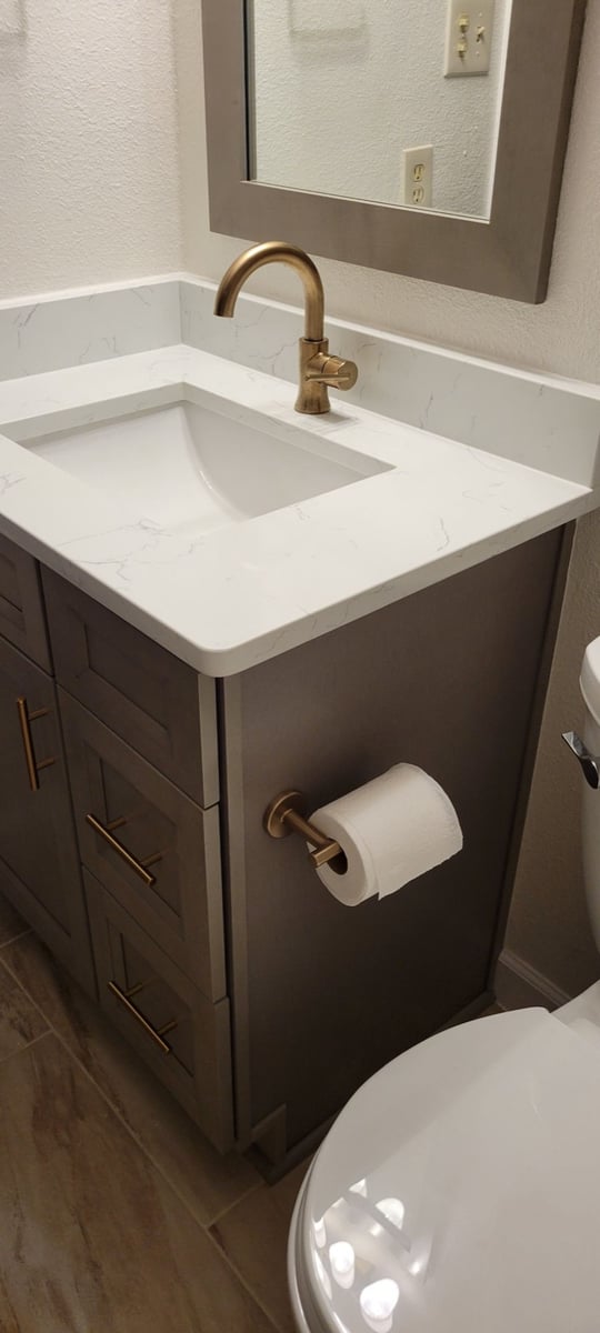 Gray vanity with white quartz top, brushed gold faucet, and matching toilet paper holder