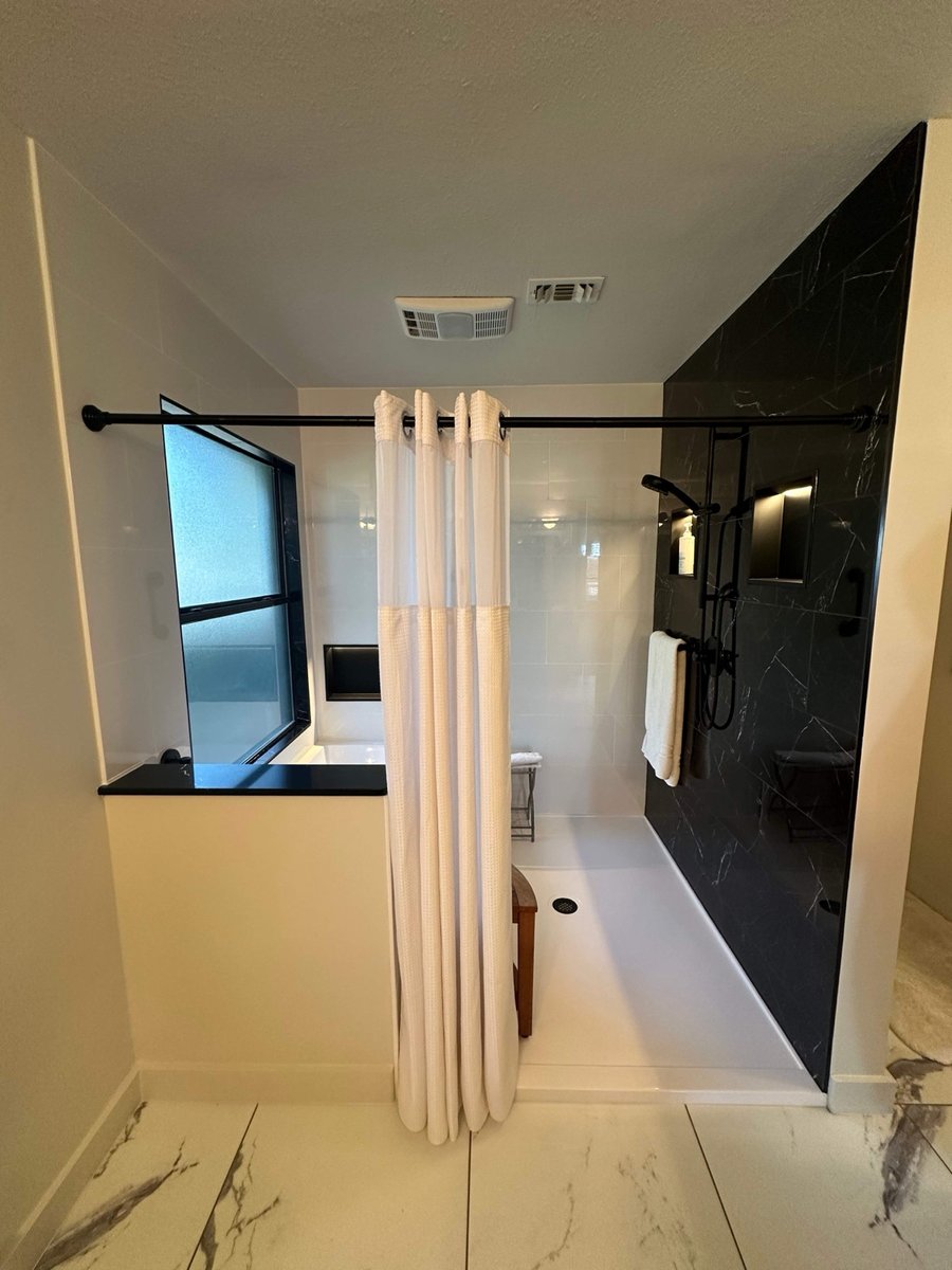 Walk-in shower split between black marble and white tile with curtain rod