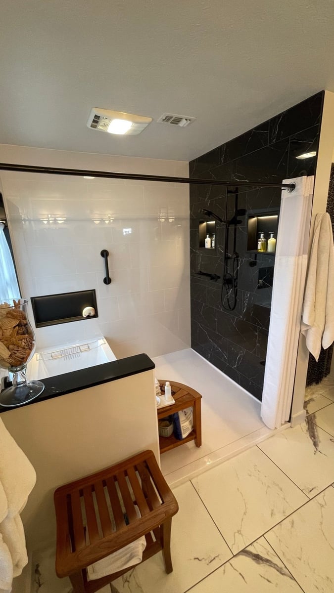 Overhead view of white tub and black marble shower with teak bench stool
