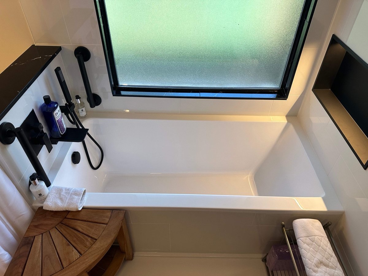 Overhead view of white drop-in tub below frosted window with teak seat