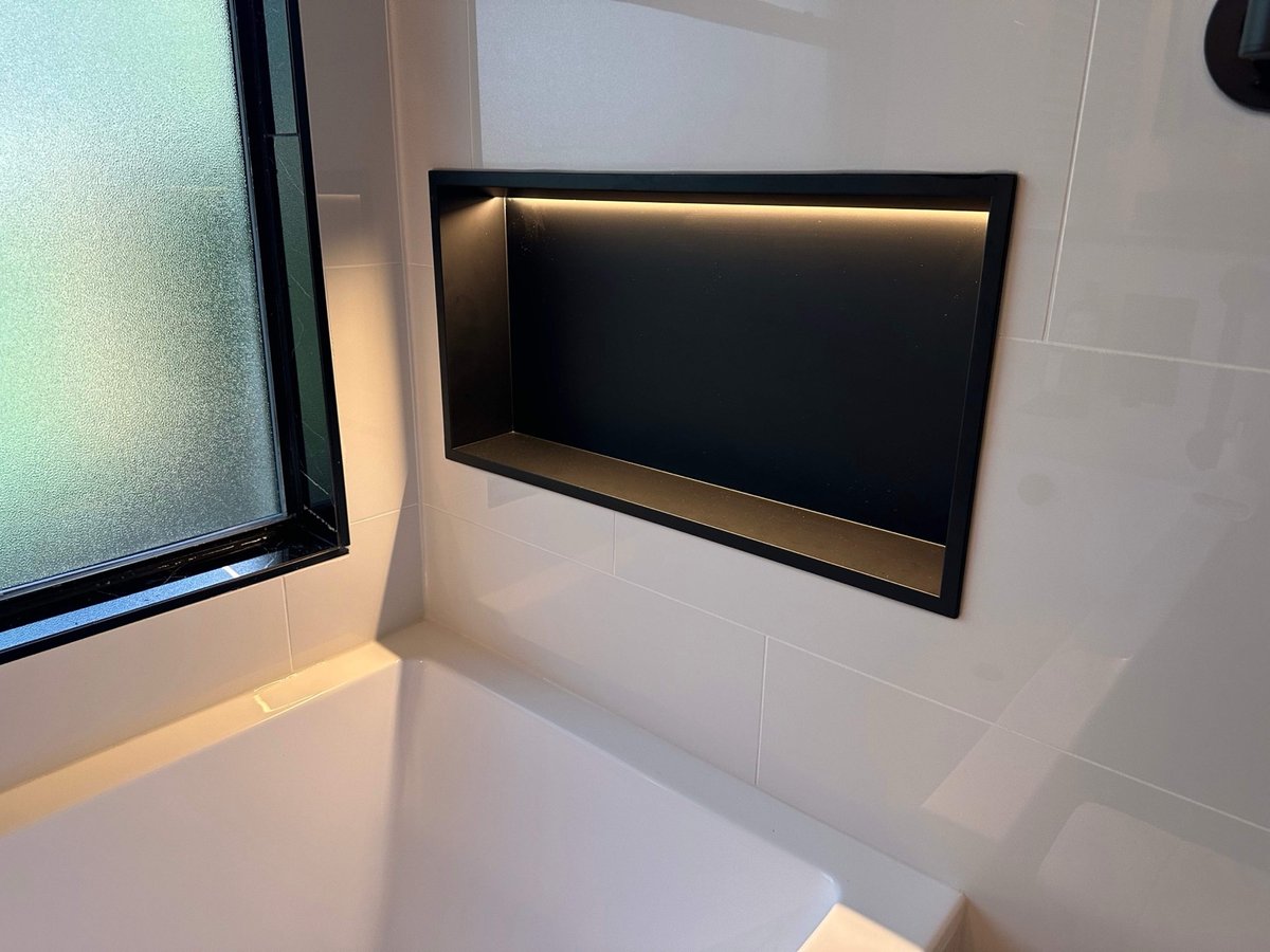 Black-framed recessed niche with backlighting set in white tile above tub