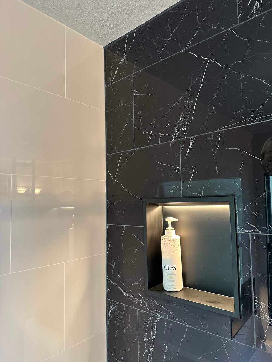 Black marble accent wall meeting white tile with lit niche holding lotion
