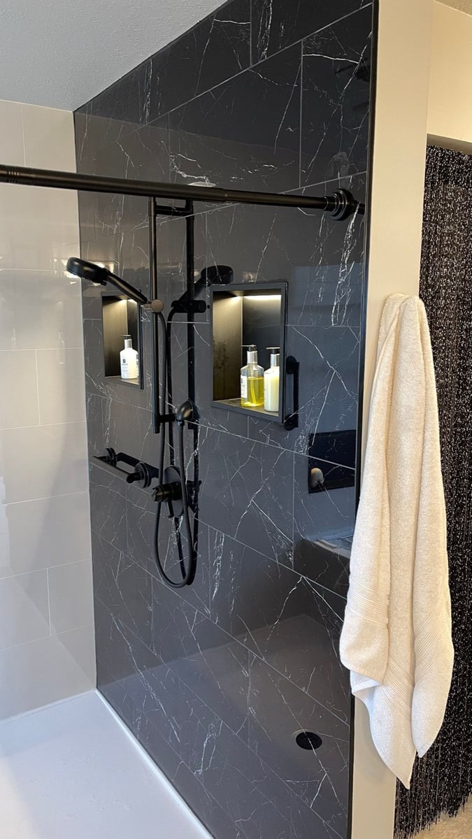 Black marble walk-in shower with matte black fixtures and white towel