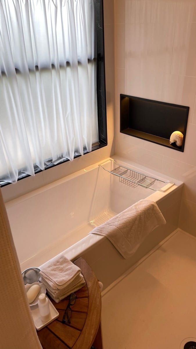 White drop-in tub by frosted window with chrome caddy and lit black niche