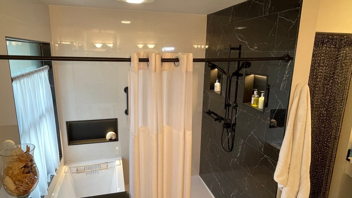 Wide view of bathroom pairing white tub and black marble curtained shower