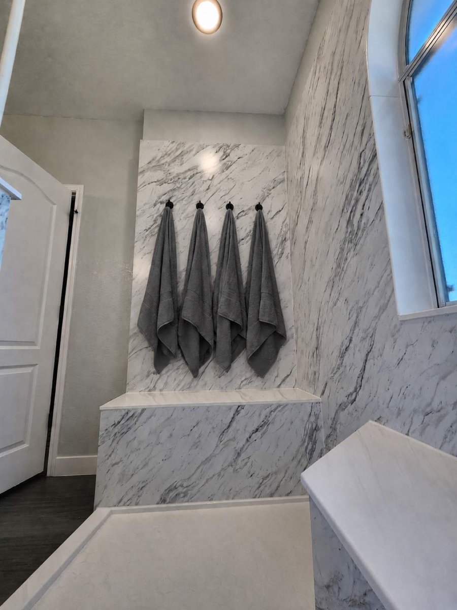Gray bath towels hanging on black hooks against marble shower wall