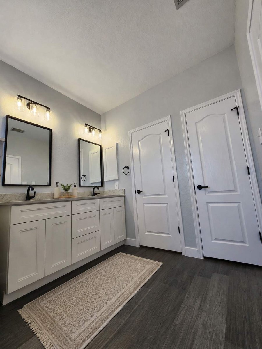 Open bathroom with white double vanity, framed mirrors, and patterned floor runner