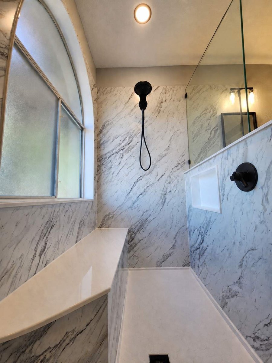 Marble shower with frosted arched window, black showerhead, and glass partition