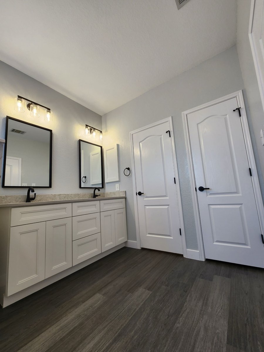 Double vanity with framed mirrors and white cabinets across from dark plank floor