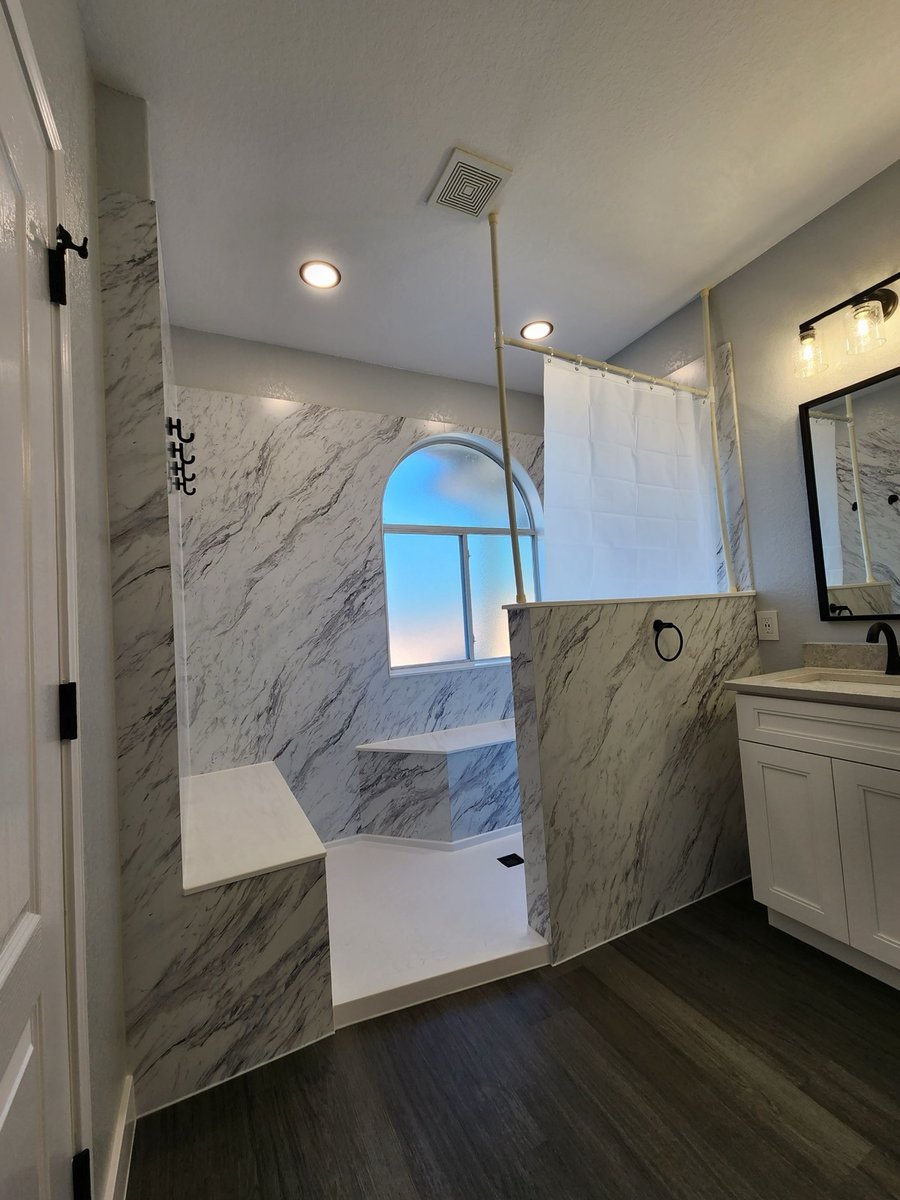 Curbless walk-in shower with marble walls, corner bench, and arched window