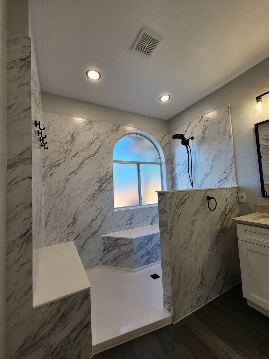 Walk-in shower with marble walls, built-in bench, and black handheld fixture