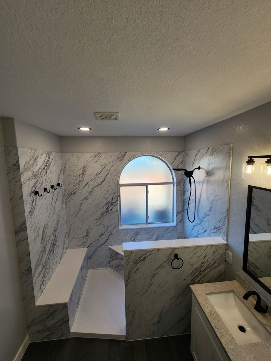 Marble walk-in shower with corner bench, towel hooks, and arched window