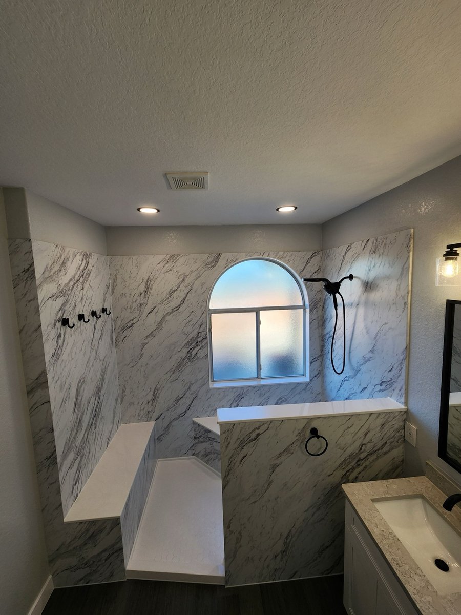 Walk-in shower with white marble walls, low partition wall, and arched window