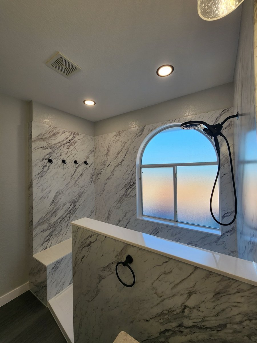 Looking up at arched shower window with black handheld and recessed ceiling lights