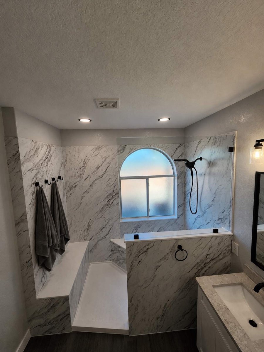 Marble walk-in shower with gray towels on hooks and built-in seating bench
