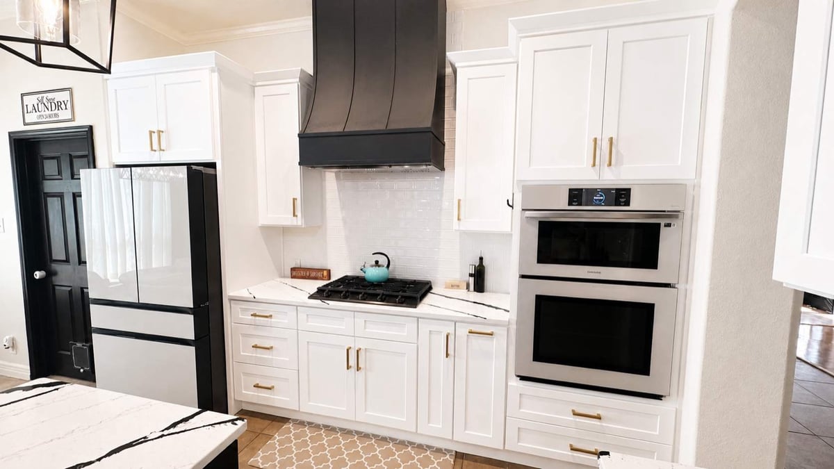 White cabinets, black hood and stainless double ovens beside French-door fridge