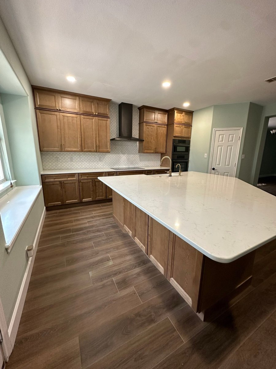 Stained wood cabinets and large white quartz island over wood-look tile flooring