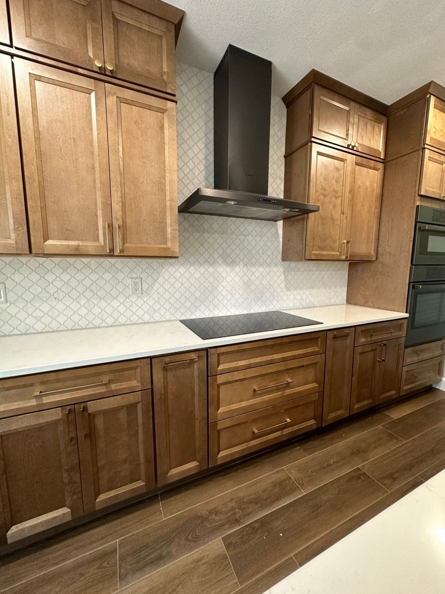 Cooktop run with black chimney hood and arabesque tile backsplash on stained cabinets