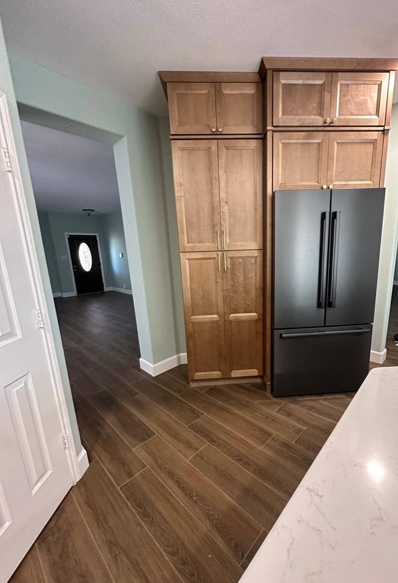 Tall pantry cabinets beside a matte black refrigerator with view to front entry