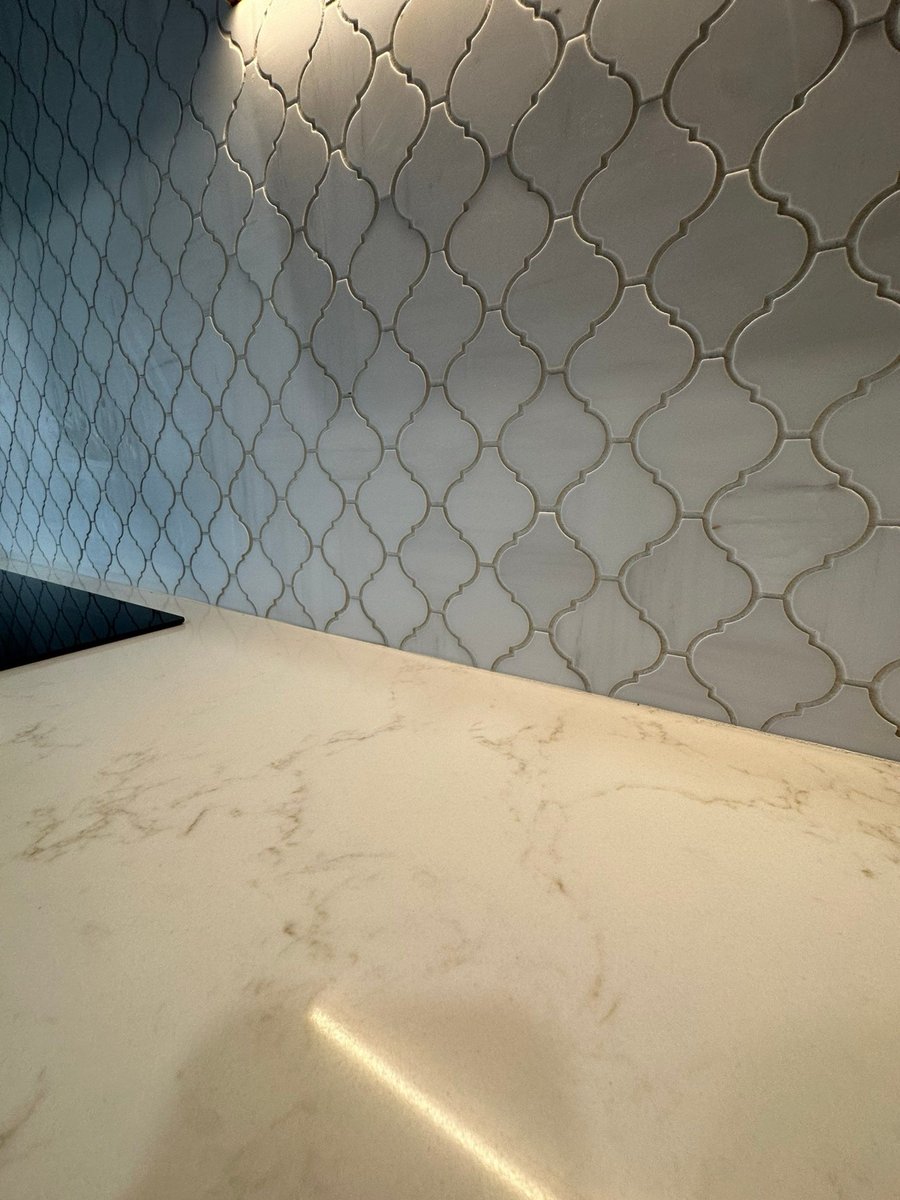 Close-up of white arabesque tile backsplash meeting veined quartz countertop