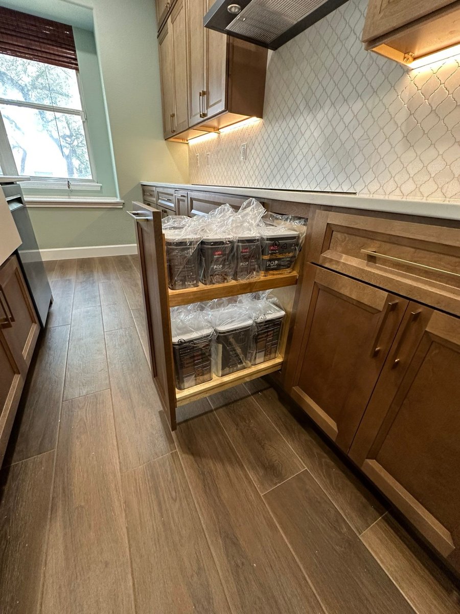 Pull-out drawer storage holding pantry bins below window and stained cabinets