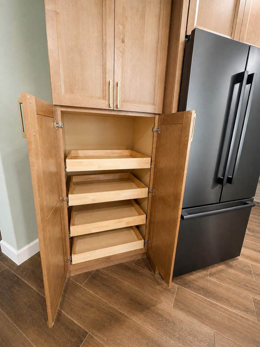 Open upper cabinet with wood roll-out shelves beside matte black refrigerator