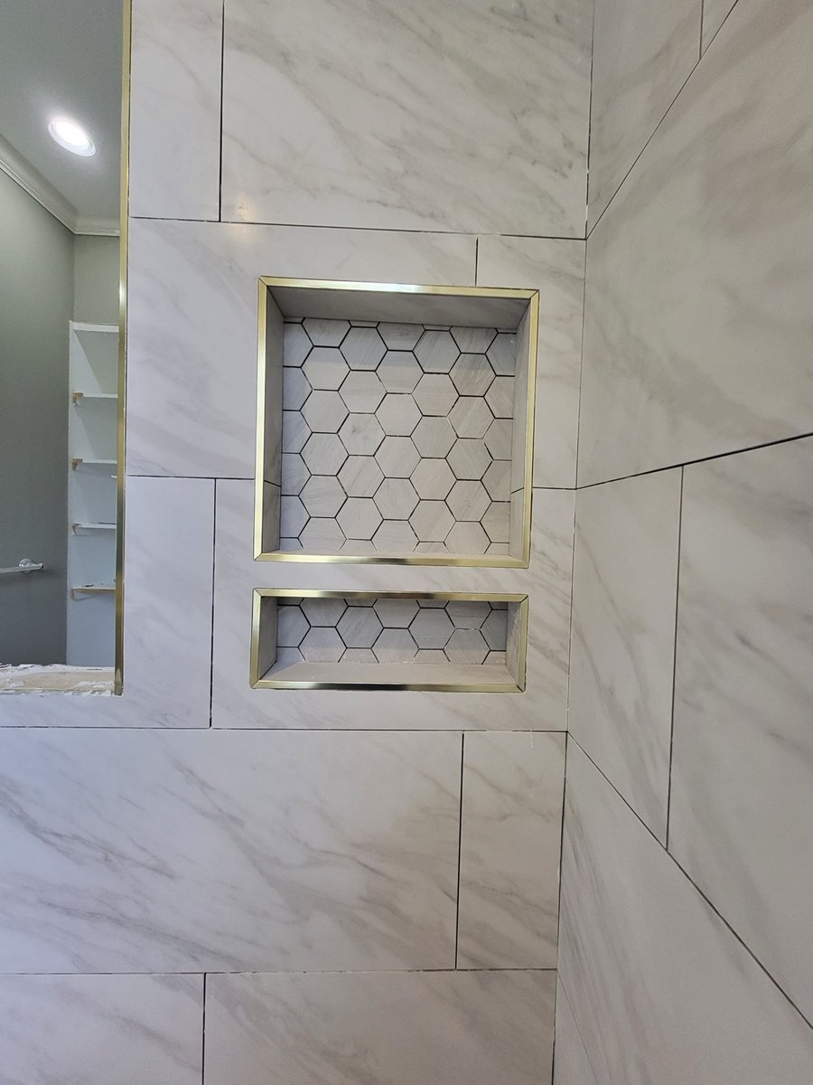 Marble-look tile shower wall with gold-trimmed double hexagon niche