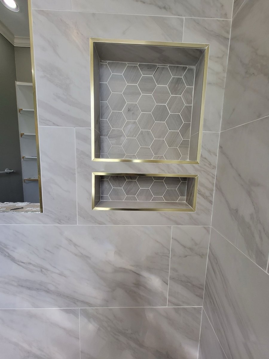 Angled view of gold-framed shower niches set in marble-look wall tile