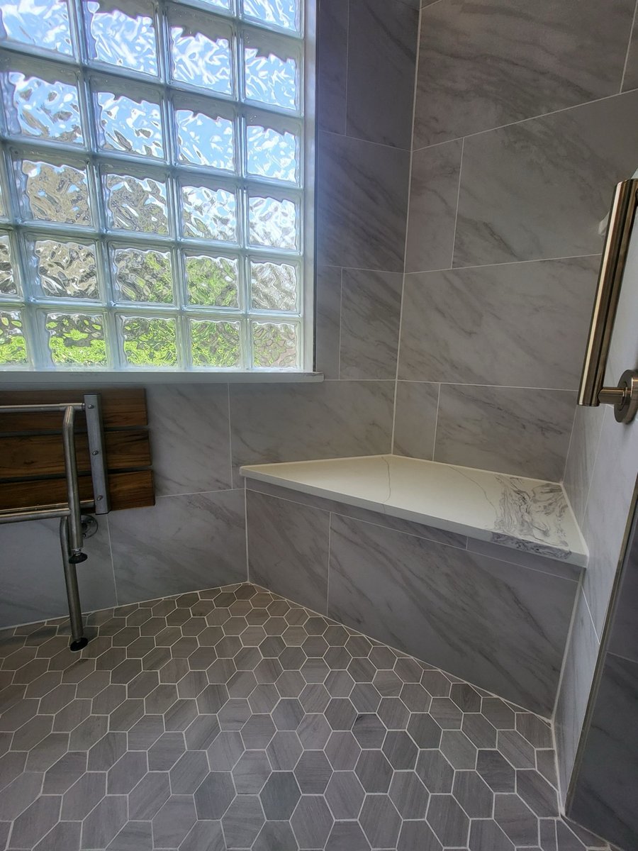 Accessible shower bench beneath a glass block window with hexagon tile floor