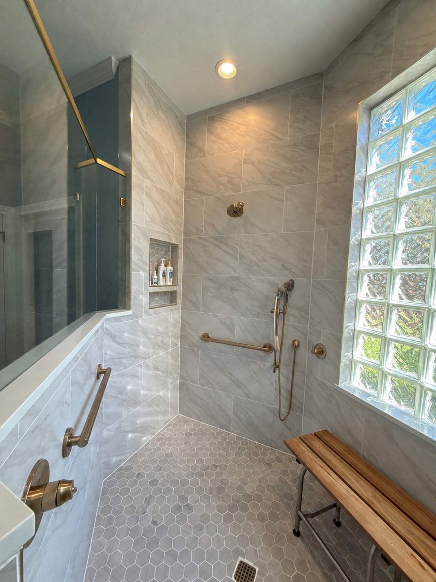 Walk-in marble shower with hand shower, grab bars, and folding teak bench