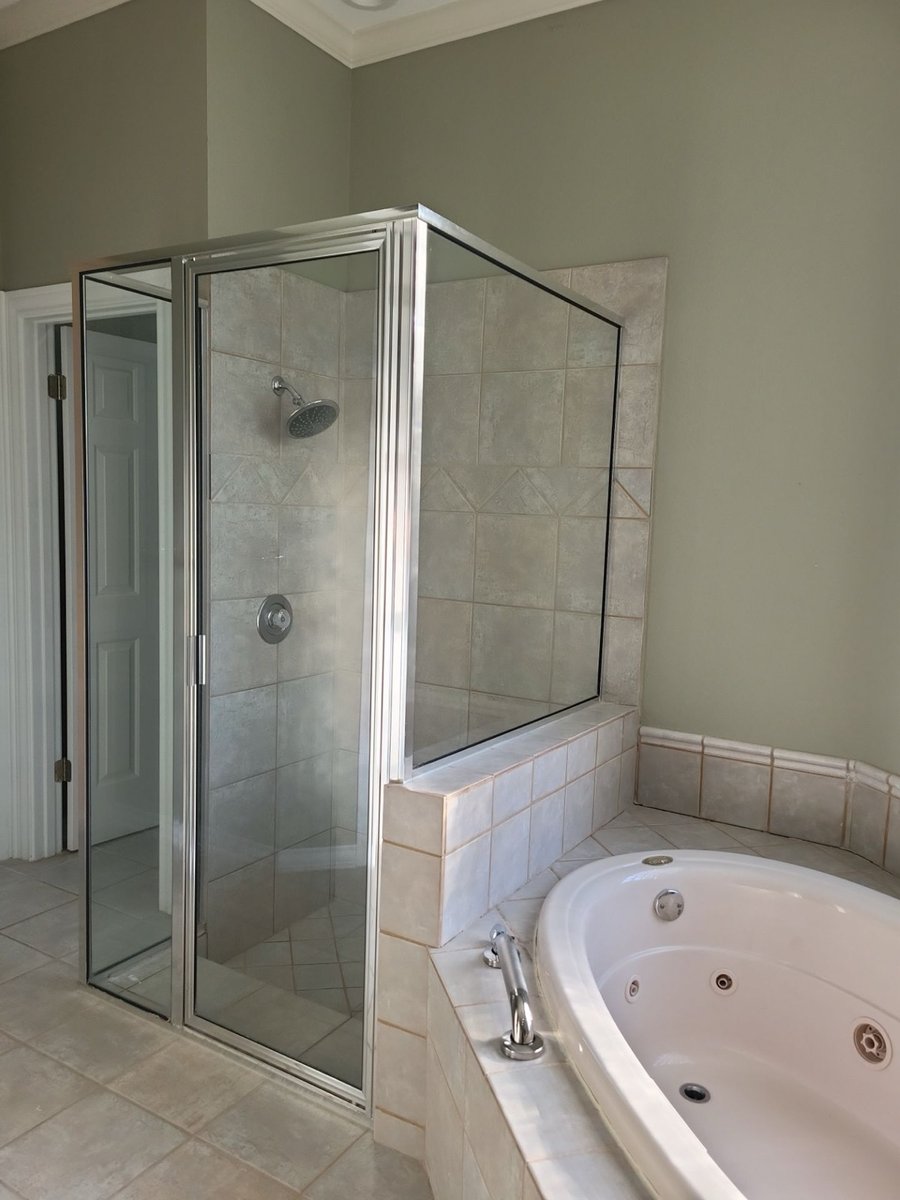 Dated framed glass shower beside a corner jetted tub before renovation