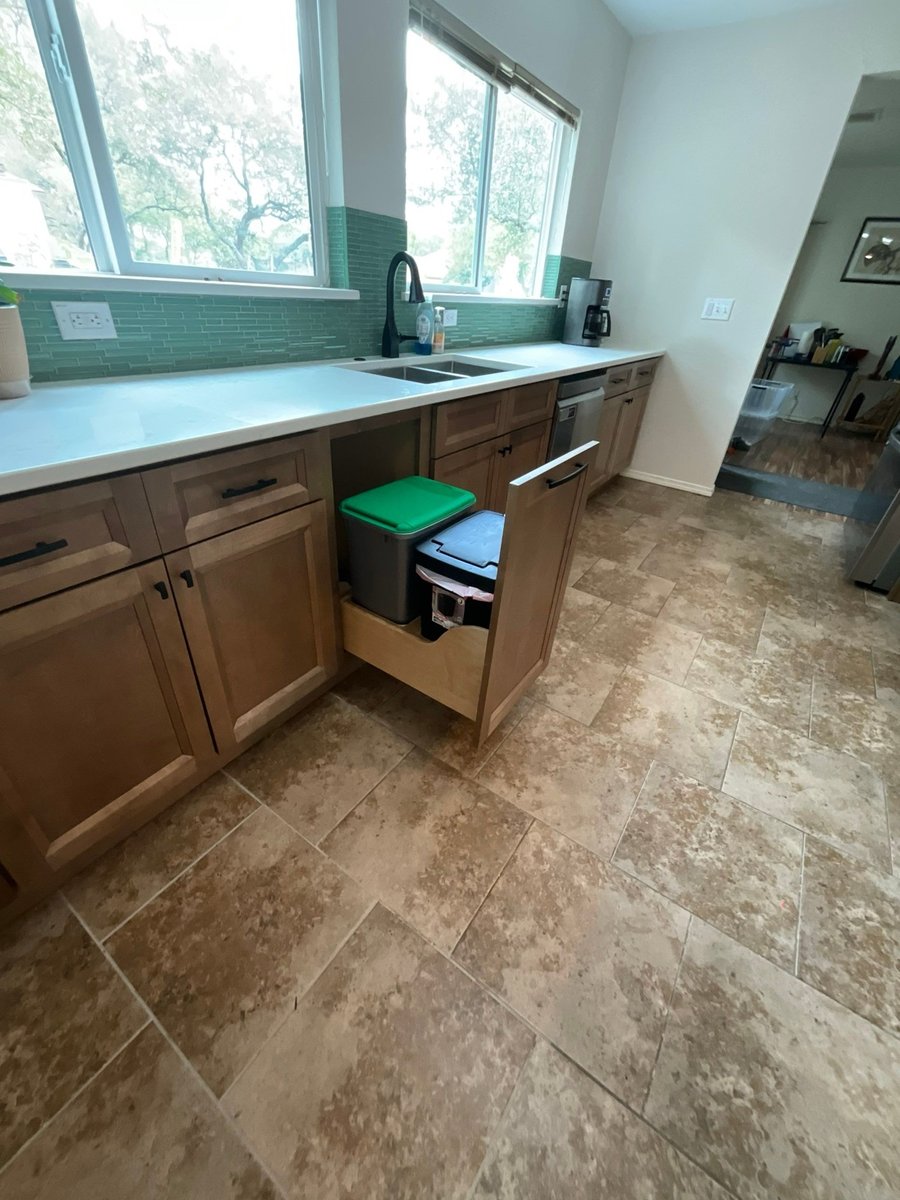 Pull-out trash and recycling drawer below counter with green tile backsplash