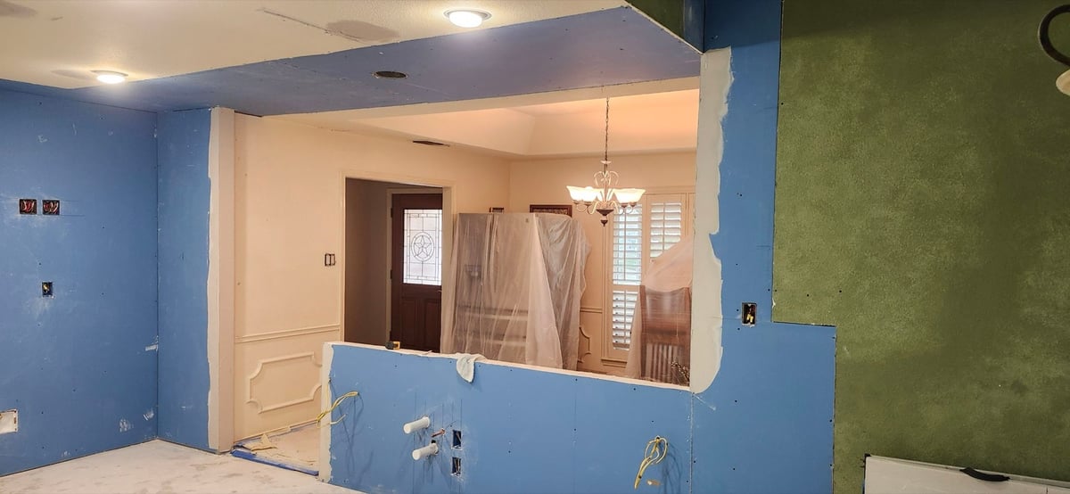 Demolished kitchen with bare drywall, blue ceiling and view to entry