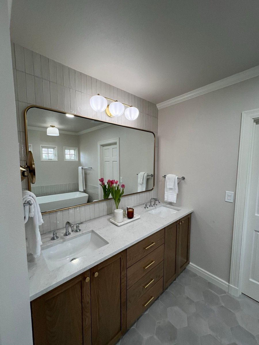 Double vanity with wood cabinets, large gold-framed mirror, and globe vanity lights