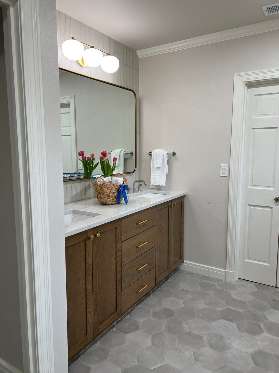 Wood double vanity with gold-framed mirror, pink tulips, and gray hexagon floor tile