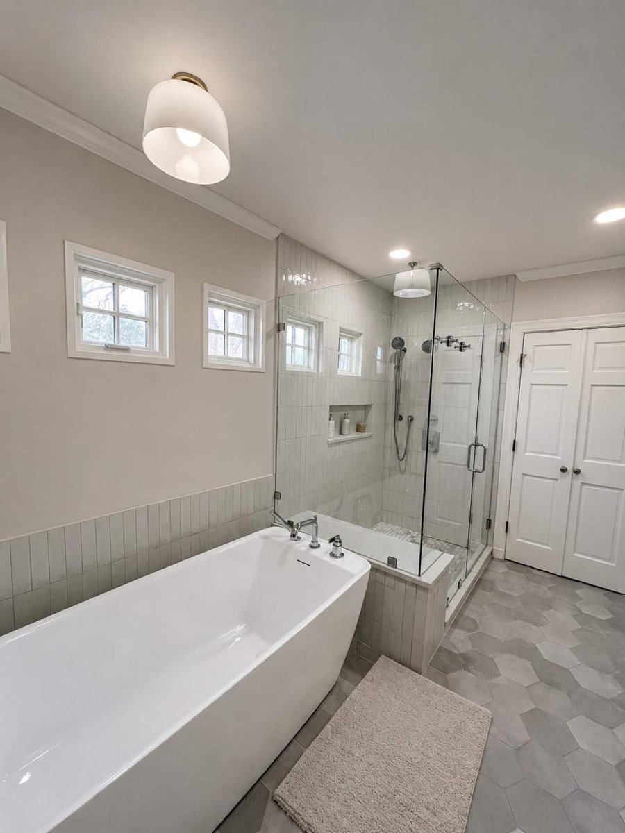 White soaking tub beside corner glass shower with white tile and clerestory windows