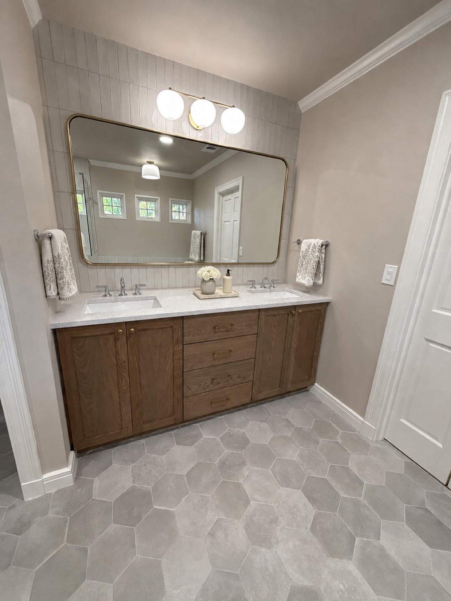 Wood double vanity with gold-framed mirror, globe lights, and gray hexagon floor