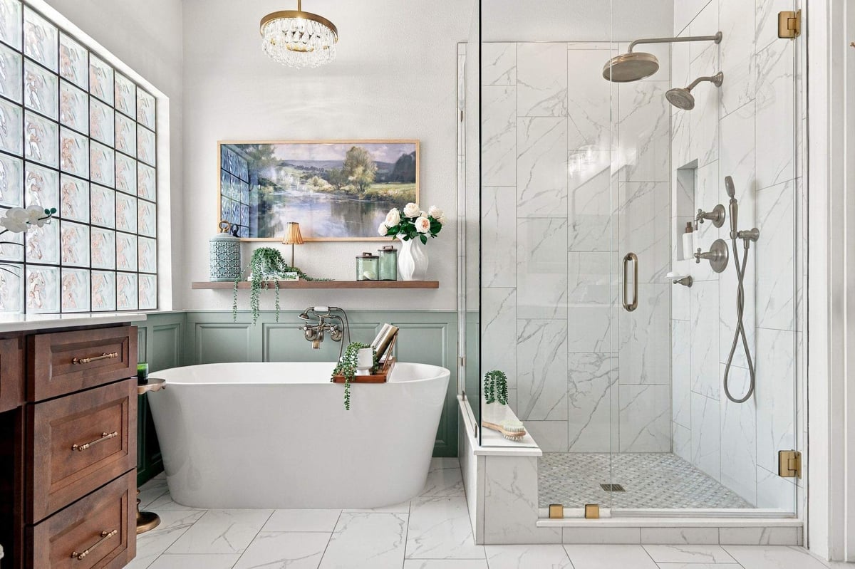 Rogers Ranch primary bathroom remodel featuring a freestanding soaking tub, spacious glass-enclosed shower, marble-look tile, and warm brass fixtures.