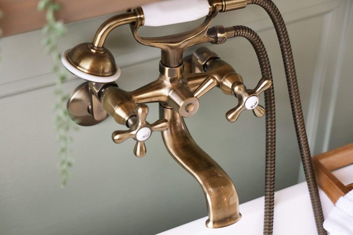 Close-up of a vintage-style brass floor-mounted bathtub faucet beside a freestanding soaking tub in a Rogers Ranch primary bathroom remodel.