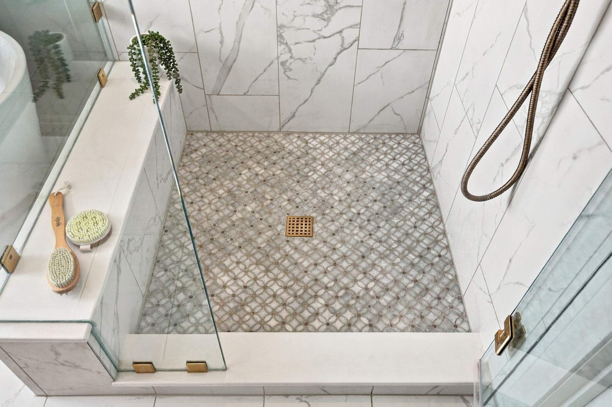 Decorative mosaic tile shower floor with marble-look wall tile and brass fixtures in a Rogers Ranch primary bathroom remodel in San Antonio.