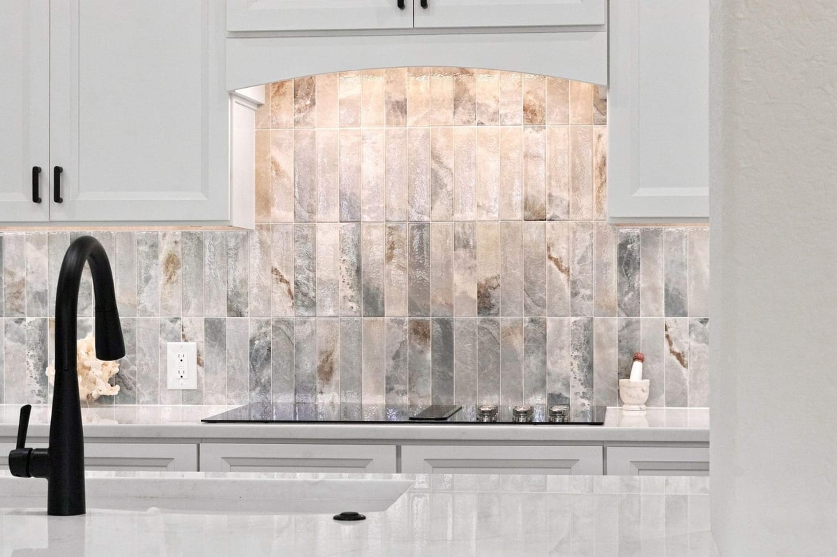 Close-up of the decorative multicolored tile backsplash, white cabinetry, and black faucet in a Cibolo Canyons kitchen remodel in San Antonio.