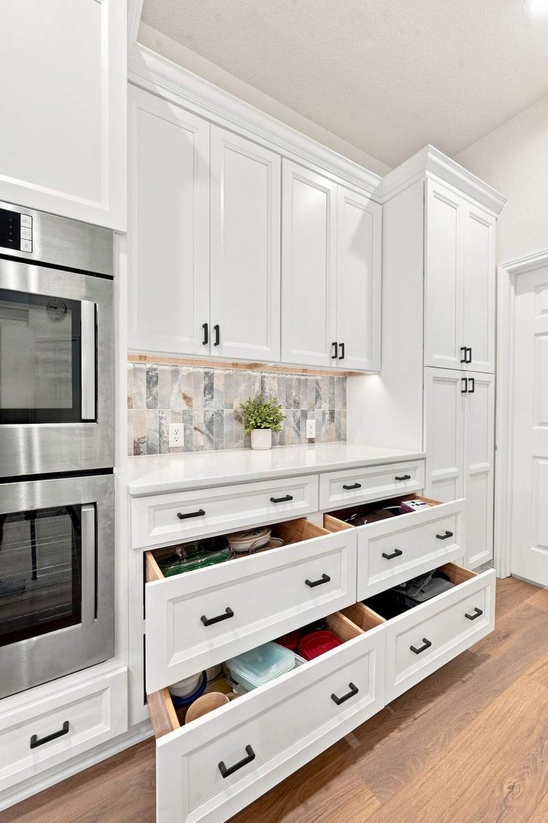 Deep pull-out storage drawers in a Cibolo Canyons kitchen remodel, featuring white shaker-style cabinetry, black hardware, and organized kitchen storage.