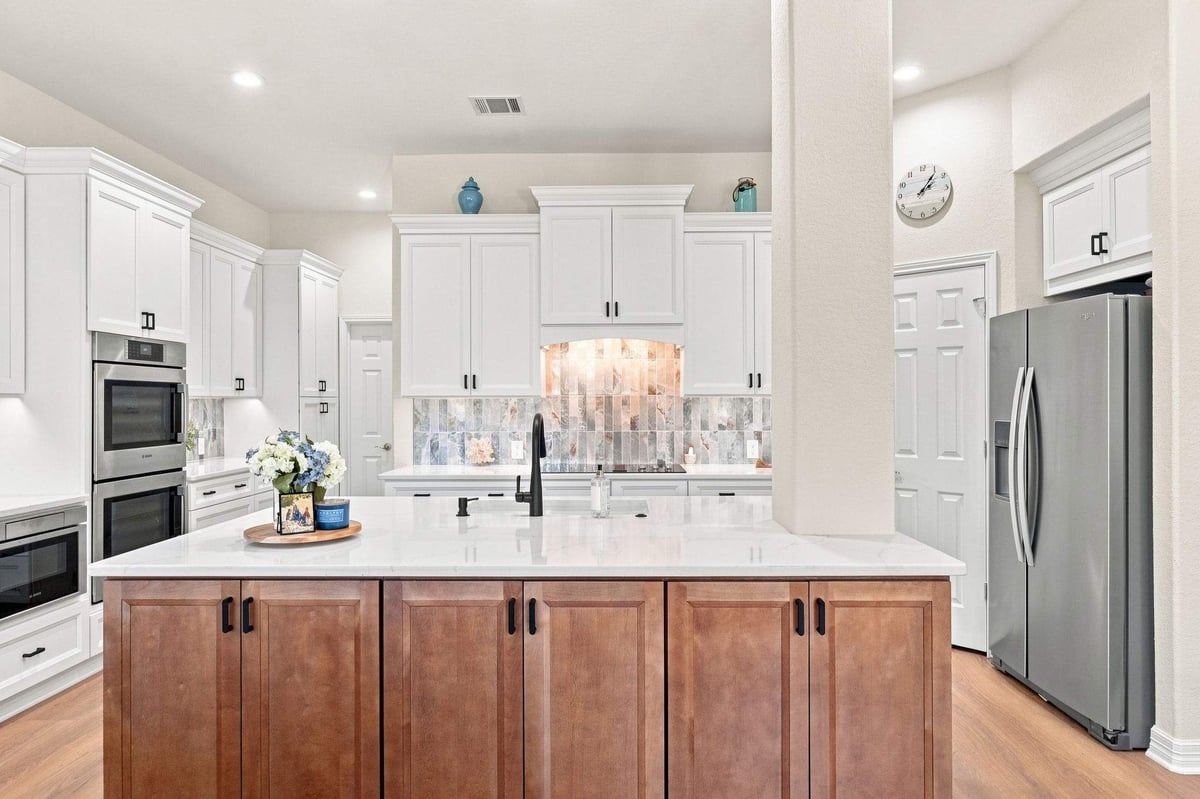 Cibolo Canyons kitchen remodel in San Antonio featuring a large wood island, white shaker-style cabinets, white countertops, and colorful tile backsplash.