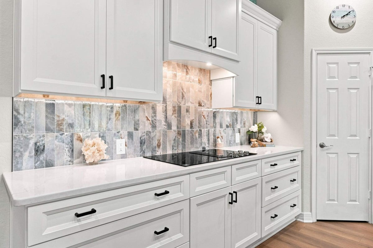 White shaker-style kitchen cabinets with matte black hardware, white countertops, and decorative tile backsplash in a Cibolo Canyons kitchen remodel.