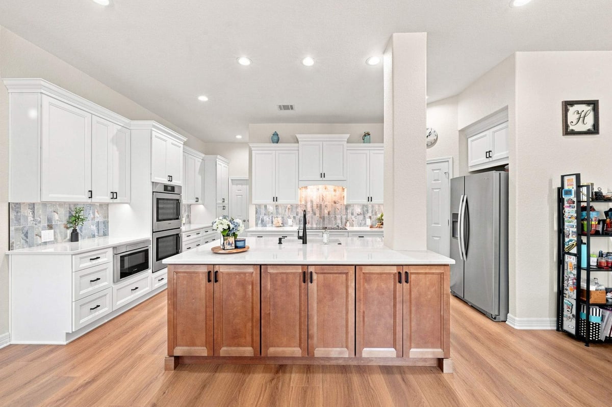 Cibolo Canyons kitchen remodel featuring a warm wood island, white cabinetry, decorative tile backsplash, and black hardware.